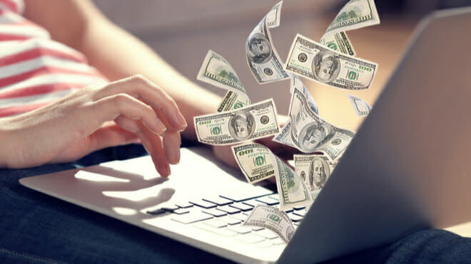 person typing on a laptop with dollar notes flying out of the screen with money earned from being a digital marketer